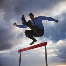 Businessman jumping over a hurdle. Photographe : Mike Kemp