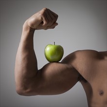 Green apple perched on a flexed muscular arm. Photographe : Mike Kemp