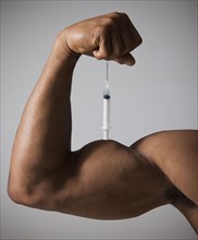 Syringe perched on a flexed muscular arm. Photographe : Mike Kemp