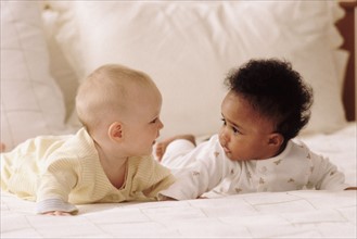 Two babies lying on a bed together. Photographe : Rob Lewine