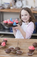Young girl holding a plate of cupcakes. Photographe : Dan Bannister