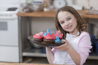 Young girl holding a plate of cupcakes. Photographe : Dan Bannister