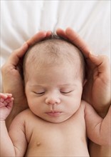 Parent's hands wrapped around sleeping baby's head.