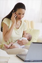 Mother talking on phone while holding her baby.