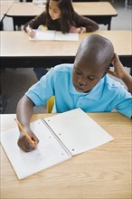 Elementary students writing in notebooks at their desks.