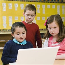 Kindergarten students looking at laptop in classroom.