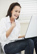 Woman looking at laptop and laughing. Photo : momentimages