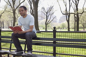 Man sitting on bench reading book in Central Park. Photo : David Engelhardt