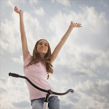 Pretty teenage girl with her arms raised while sitting on bike. Photo : Mike Kemp