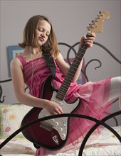 Young girls playing guitar on her bed. Photo : Mike Kemp