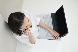 Woman talking on phone while holding laptop. Photo : momentimages