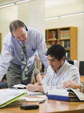 College professor helping college student in library.