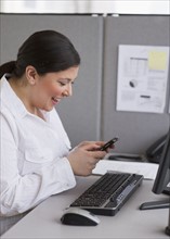 Businesswoman texting at her desk in cubicle.