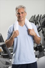 Man at the gym standing with towel around his neck.