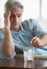 Man with a headache putting medicine in glass of water.