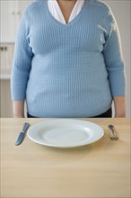 Overweight woman standing in front of place setting.