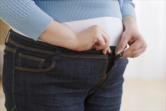 Overweight woman buttoning up her jeans.