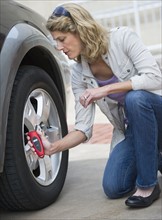 Woman using pressure gauge to check tire pressure.