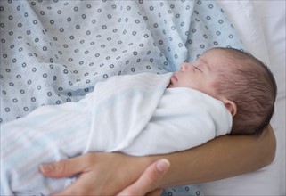 Newborn baby swaddles in mother's arms.