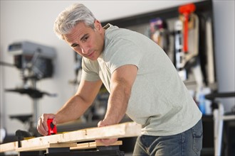 Handyman measuring a piece of wood in workshop.