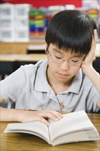 Elementary school student reading book at desk.