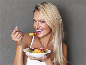 Blond woman eating fresh fruit salad. Photo : momentimages