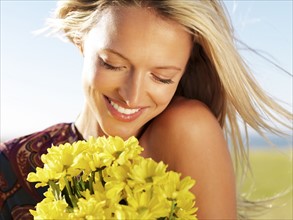 Blond woman holding yellow flowers. Photo : momentimages