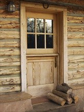 Firewood in front of door of log cabin. Photo : John Kelly