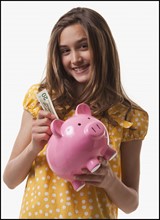 Teenage girl putting money in piggy bank. Photo : Mike Kemp