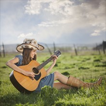 Cowgirl playing guitar in field. Photo : Mike Kemp