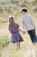 Young boy and girl walking hand in hand in meadow. Photo : Rob Lewine