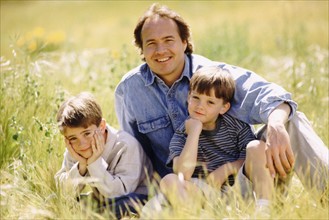 Father and his two sons sitting in meadow together. Photo : Rob Lewine