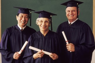 Three adult students wearing graduation gowns. Photo : Rob Lewine