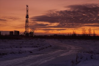 Snowy road at dusk with oil drilling rig in background. Photo : Dan Bannister