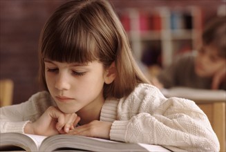 Elementary school student reading book at her desk. Photo : Rob Lewine