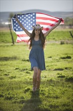 Beautiful cowgirl running with American flag in her arms. Photo : Mike Kemp