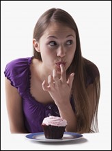 Woman sneaking a lick of icing from a cupcake. Photo : Mike Kemp
