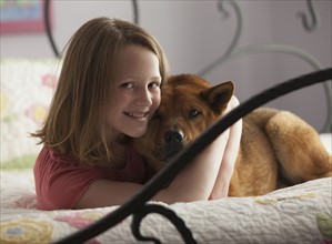 Young girl hugging dog on bed. Photo : Mike Kemp