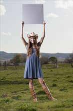 Cowgirl holding up blank poster while standing in field. Photo : Mike Kemp