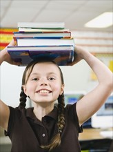 Elementary student holding a stack of books on her head.