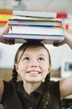 Elementary student holding a stack of books on her head.