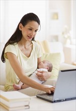 Mother typing while holding baby.
