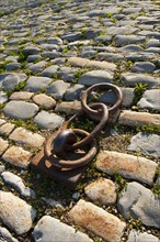 Rusty chain anchored to the ground amongst cobblestones.