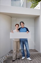 Couple standing in front of their home. Photo. momentimages