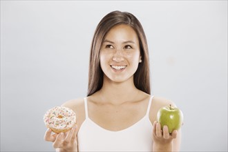 Woman holding an doughnut and an apple. Photo. FBP