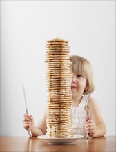 Young girl sitting behind a tall stack of pancakes. Photo : FBP