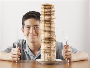 Young boy sitting behind a tall stack of pancakes. Photo. FBP