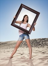 Woman standing on beach holding picture frame. Photo. Mike Kemp