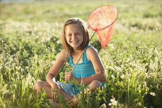 Young girl sitting in field with a butterfly net. Photo. Mike Kemp