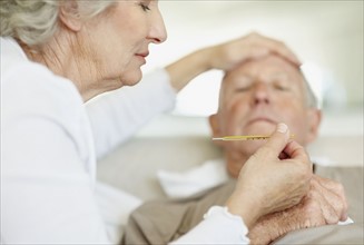 Senior woman caring for man with a fever. Photo : momentimages